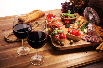 Traditional italian antipasto bruschetta appetizer with cherry tomatoes, cream cheese, basil leaves and balsamic vinegar on cutting board with prosciutto, salami, cheese