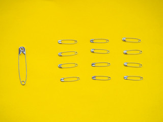 A large safety pin followed by other smaller ones in human representation. Leadership concept