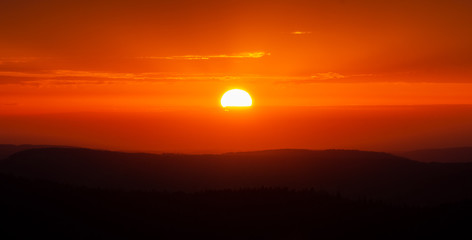 Scenic sunset over mountains. Glowing sun and orange sky and mountain range scenery or landscape.