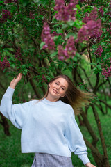 A girl with brown eyes and flying hair and lilac bloom in May 2019