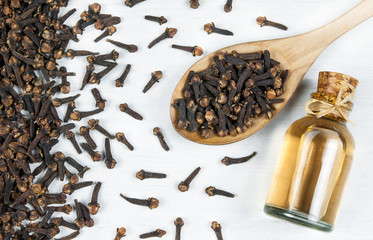 Close up glass bottle of clove oil and cloves in wooden spoon on white rustic table. Essential oil...
