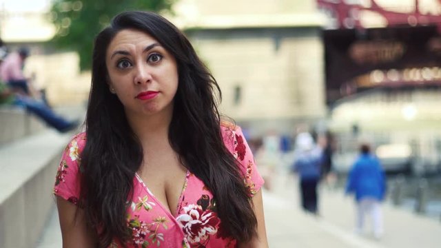  Young Latina woman  talking head is at Chicago River Walk  having an exciting conversation and happy showing many facial expression while moving hair.  wearing pink blouse