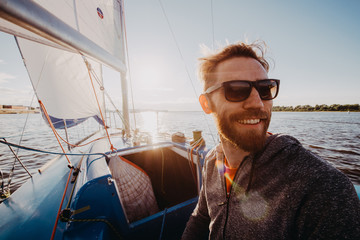 A handsome bearded man in sunglasses on a boat on a river or lake. Beautiful happy guy swimming in a boat on a autumn sunny day feeling free enjoying life - 268248347
