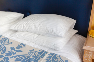 White pillows on the bed comfortable soft pillows on the bed in a stylish hotel room. Pillows lie on top of each other on a tucked-in bed with a blue headrest