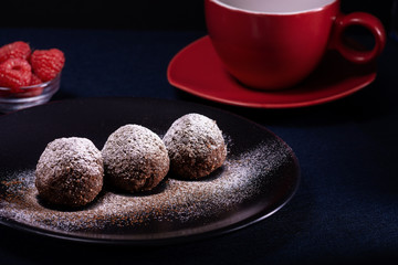 Homemade chocolate cake balls truffels sprinkled with powder sugar on black plate and red and black  raspberry with coffe cup   with dark background in rustic style.