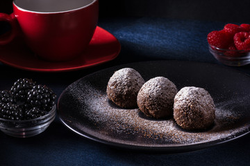 Homemade chocolate cake balls truffels sprinkled with powder sugar on black plate and red and black...