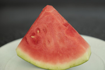 The triangular slice of watermelon lies on a white ceramic plate on a black background.