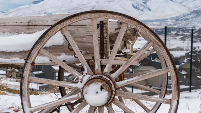 Panorama Rusty wheel of a wooden cart against a rocky ground covered with snow in winter