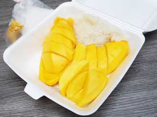 Mango sticky rice in foam box on wood table