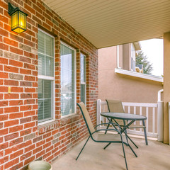 Fototapeta na wymiar Square Front porch of a home with table and chairs in front of brick wall and window