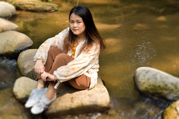 Cute asian girl sitting on stone in rural river