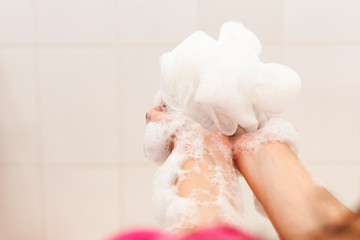 Fototapeta na wymiar Woman washing hands with a sponge in the bathroom. Female washing arms with a foamy sponge in the bath. Body care and clean concept