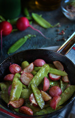 roasted young pods of peas and radish in a frying pan. light background. Soft focus