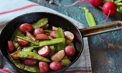roasted young pods of peas and radish in a frying pan. light background. Soft focus