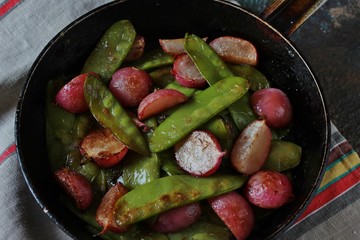 roasted young pods of peas and radish in a frying pan. light background. Soft focus