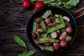 roasted young pods of peas and radish in a frying pan. light background. Soft focus