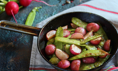 roasted young pods of peas and radish in a frying pan. light background. Soft focus