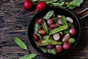 roasted young pods of peas and radish in a frying pan. light background. Soft focus