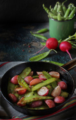 roasted young pods of peas and radish in a frying pan. light background. Soft focus