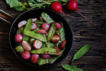 roasted young pods of peas and radish in a frying pan. light background. Soft focus