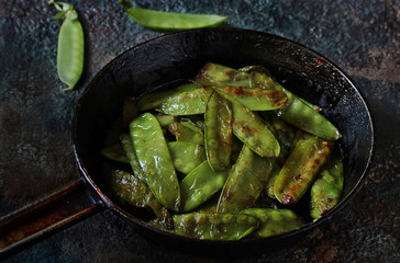 Fried young peas in a pan on a dark background.