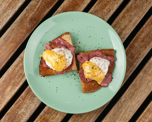 Russian crepes with poached egg, grilled bacon, cheese and herbs served on a bright turquoise plate