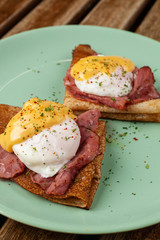 Close up of russian pancakes blini with poached egg, grilled bacon, cheese and herbs on turquoise