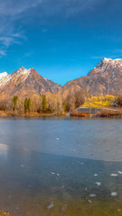 Vertical Scenic panorama of a lake against snow capped mountain and blue sky in winter