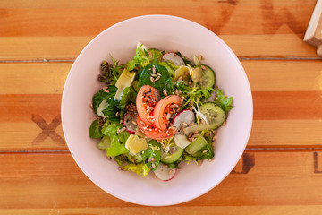 Summer vegetable salad with tomatoes, cucumbers and greens on a rustic wooden table