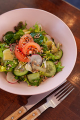 Close up of salad with fresh tomatoes, cucumbers and greens on a dark wooden table