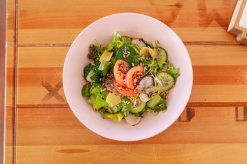 Summer vegetable salad with tomatoes, cucumbers and greens on a rustic wooden table