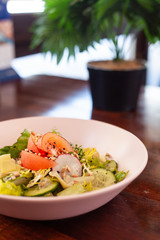 Vegan summer salad with fresh tomatoes, crunchy cucumbers and greens on a dark wooden table with cutlery on it