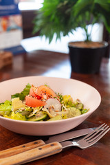 Vegan summer salad with fresh tomatoes, crunchy cucumbers and greens on a dark wooden table with cutlery on it