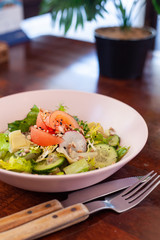 Vegan summer salad with fresh tomatoes, crunchy cucumbers and greens on a dark wooden table with cutlery on it