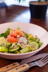 Vegan summer salad with fresh tomatoes, crunchy cucumbers and greens on a dark wooden table with cutlery on it