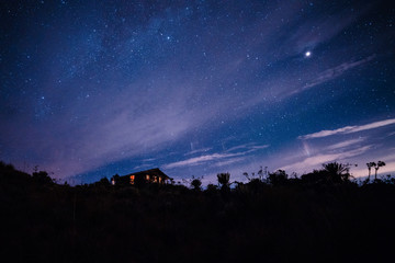 Starry night on the summit of a moor with a cottage with the lights on