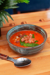 Summer seasonal gazpacho with herbs, tomatoes and basil  on a tropical background and wooden bali table