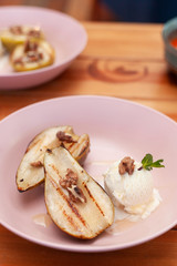 Sweet BBQ dessert: grilled pears with walnuts and a nice scoop of vanilla ice cream on a light wooden table