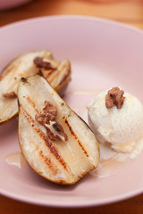 Sweet BBQ dessert: grilled pears with walnuts and a nice scoop of vanilla ice cream on a light wooden table