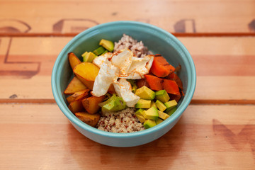 Hawaiian poke bowl with avocado, tomatoes, quinoa, rice, potato and grilled pumpkin on a wooden...