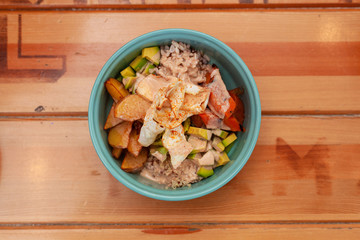 Hawaiian poke bowl with avocado, tomatoes, quinoa, rice, potato and grilled pumpkin on a wooden table