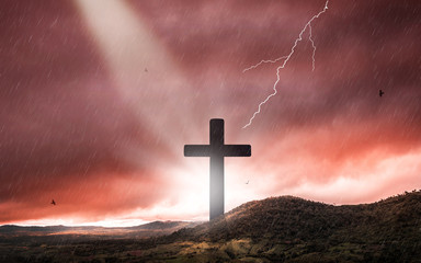Silhouette of crucifix cross at sunset time with holy light and thunderstorm background.