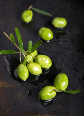 green olives and olive branch on a dark wooden board