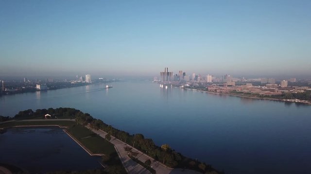 View of the Detroit skyline from Belle Isle on the Detroit river. Lake freighter passing by on a sunny summer day with blue sky. Aerial drone video of Michigan.