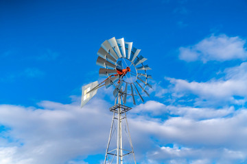 Shiny steel windpump against a vibrant blue sky with cottony clouds