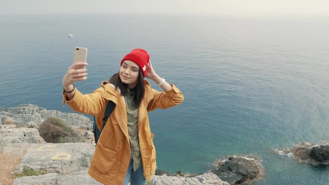 Tourist girl standing on the edge of a cliff and shooting selfie with a beautiful view on background. Cloudy autumn day. 4K