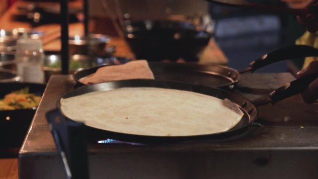 Slow motion shot of a pan with a pancake on it being moved by a hand in a street market.