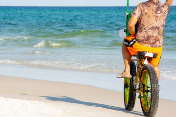 Fototapeta premium Man Riding a Bycicle on White Sand on Blur Ocean Water Background. Destin Beach, Florida