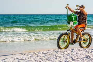 Fototapeta premium Man Riding a Bycicle on White Sand on Blur Ocean Water Background. Destin Beach, Florida