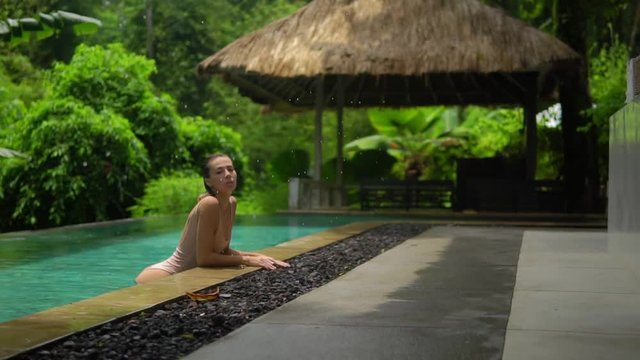 amaizing shooting raindrops fall onto open swimming pool with nice girl in it,